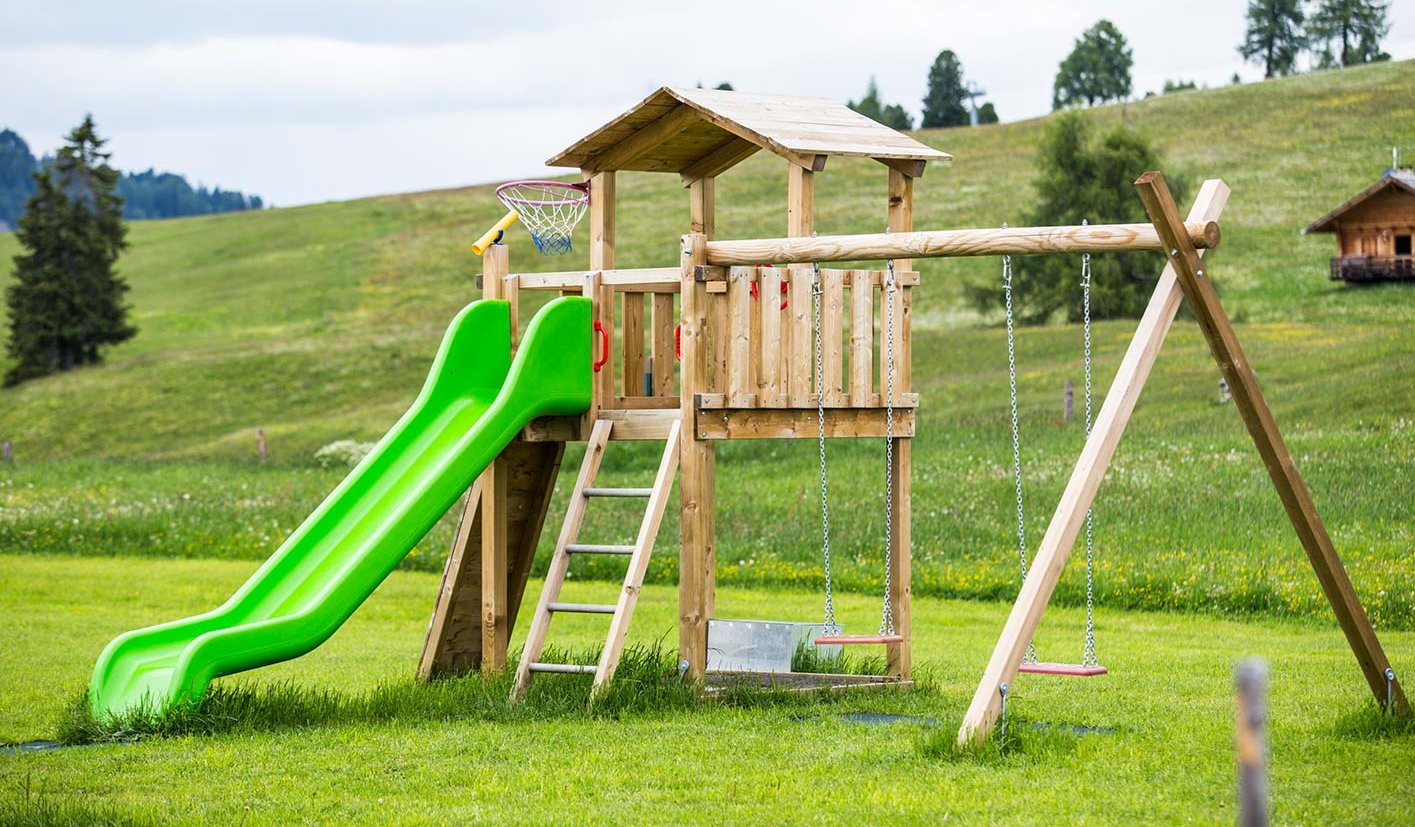Ein Holzspielturm mit Rutsche und Schaukel auf einer großen Wiese